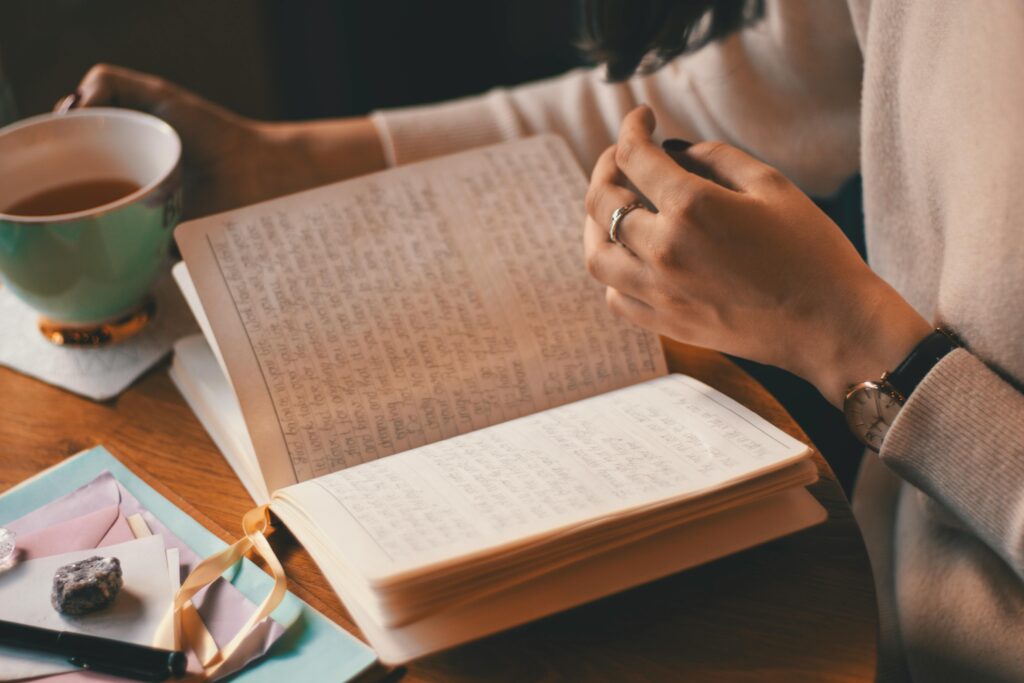 A woman writes in a journal while enjoying a cup of coffee at a wooden table.