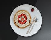 A tempting pancake topped with fresh bananas and strawberries on a white plate. Perfect for breakfast or dessert.