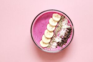 Colorful açaí smoothie bowl with banana, chia seeds, and more on pink background.