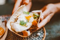 A close-up view of a breakfast taco with egg, cilantro, and cheese in hands.